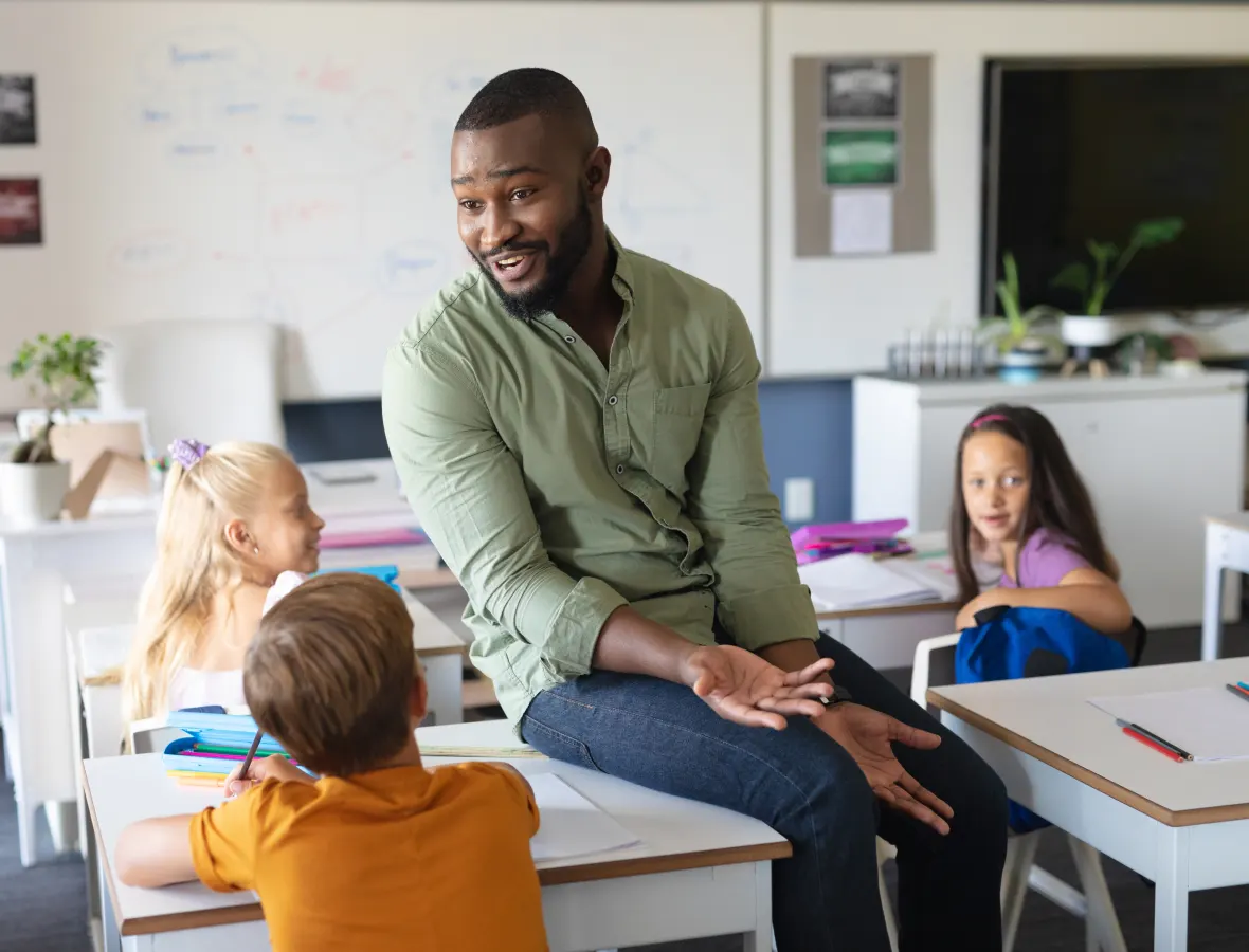 Teacher sitting on desk chatting to kids