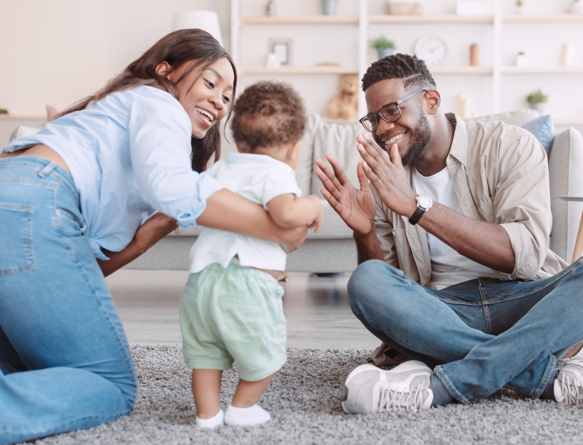 A mother and father helping their bay walk in their living room