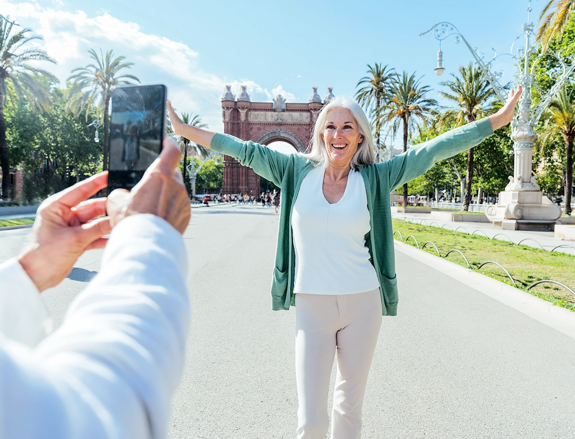 A person taking a photo of a mature woman with arms up