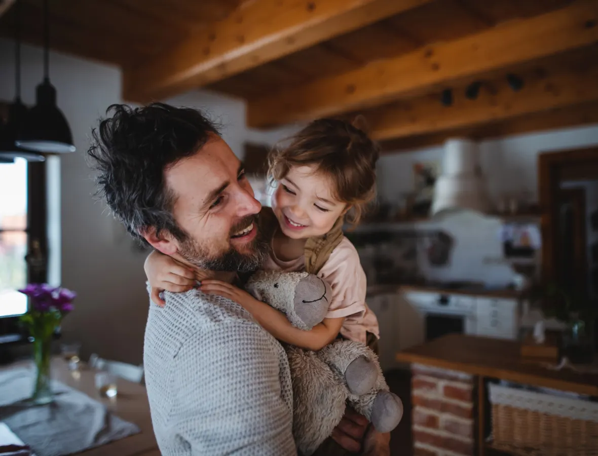 Father holding daughter and stuffed animal in kitchen