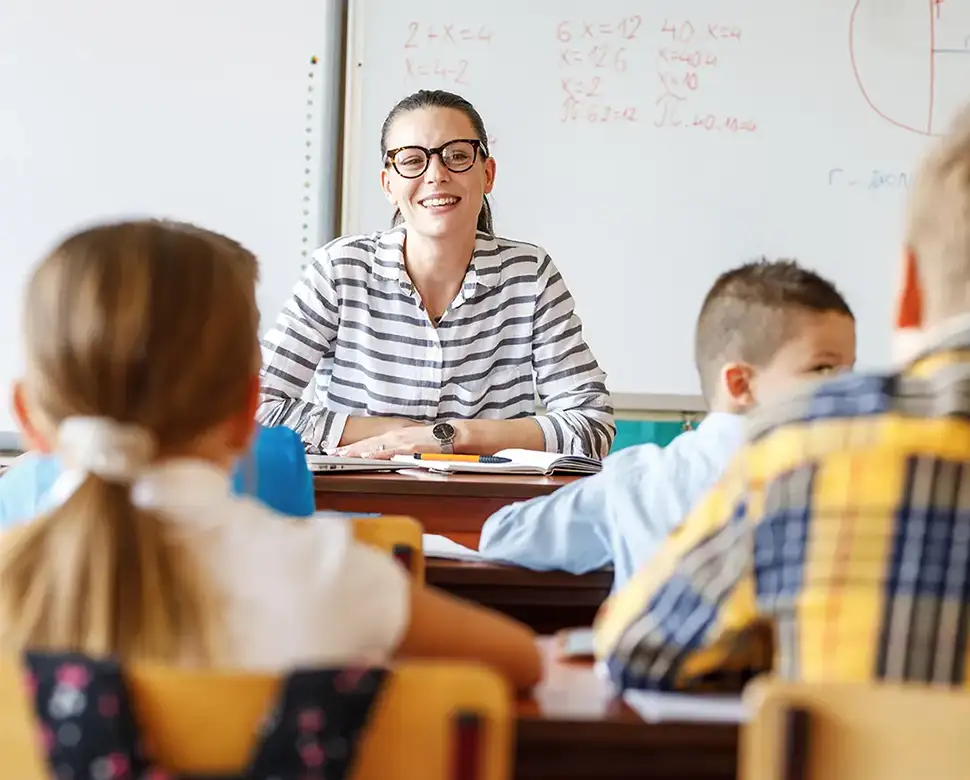 Teacher at her desk talking to young students