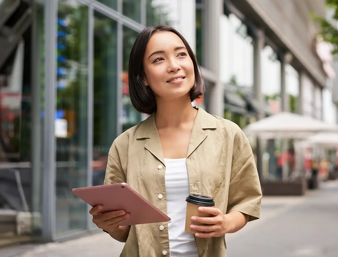 lady holding coffee and tablet walking on the street, smiling